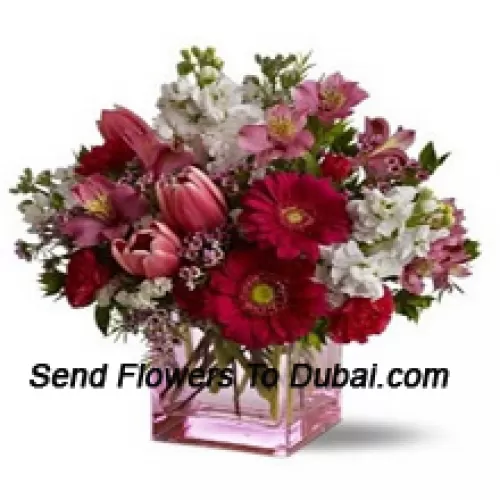 Rosas vermelhas, tulipas vermelhas e flores variadas com complementos sazonais dispostos lindamente em um vaso de vidro